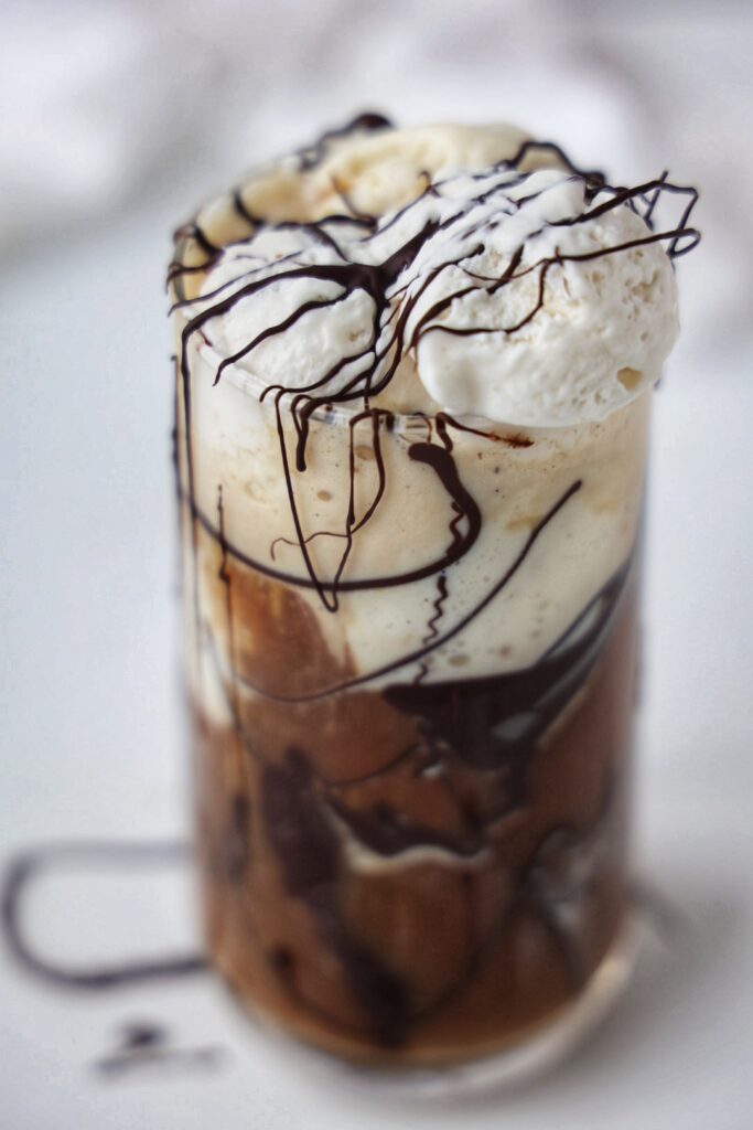 A cold brew ice cream float made with vegan ice cream, cold brew poured over the top, with chocolate drizzle around the glass and whipped cream on top.