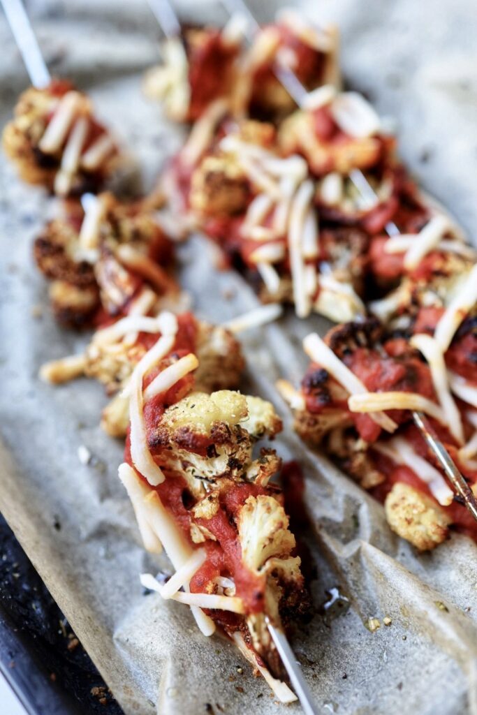 Skewers of cauliflower covered with pasta sauce and shredded cheese.