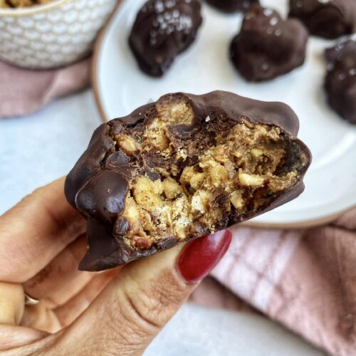 A bite out of a granola crunch bite that is covered in chocolate.
