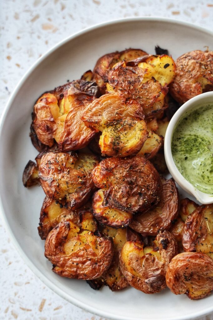 A plate of crispy garlic smashed potatoes with pesto aioil dipping sauce.