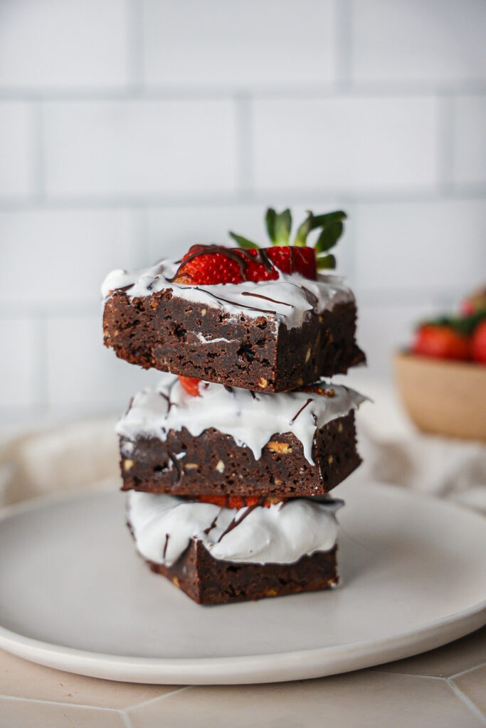 a stack of paleo brownies with coconut whipped cream and strawberries.