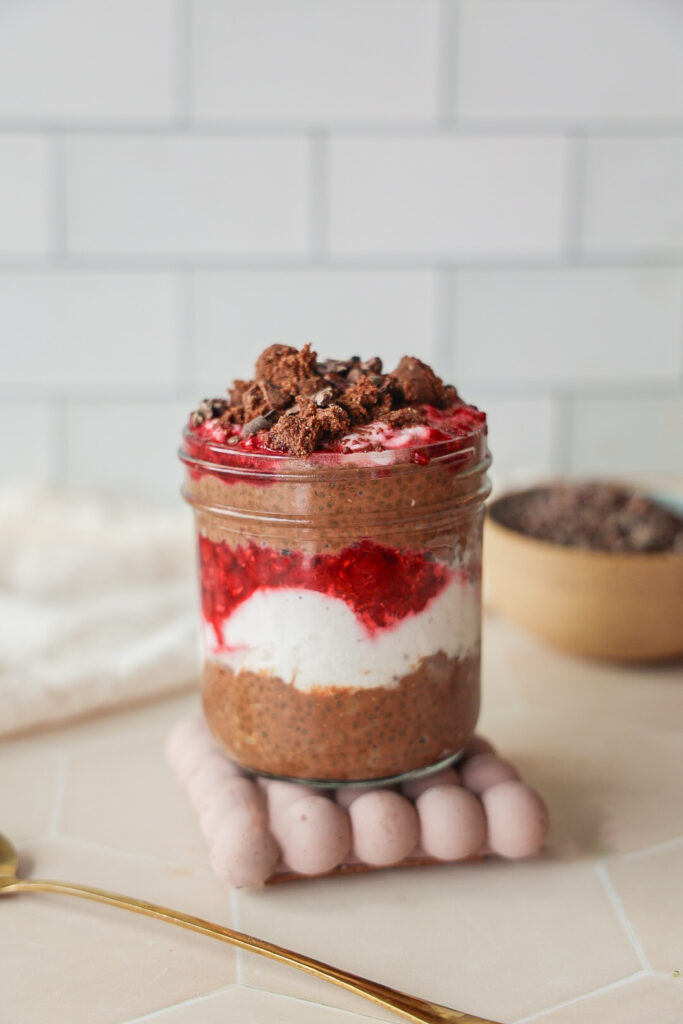 a jar of chocolate chia seed protein pudding with coconut yogurt and raspberries.